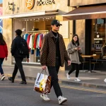 Fashionably dressed individual showcasing stylish 레플리카 clothing in urban setting with vibrant storefronts.